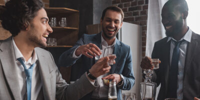 smiling multiethnic male friends in suits drinking tequila together